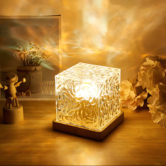 Decorative 3D glass light cube emitting a warm glow on a wooden table, enhancing a cozy ambiance with background flowers and artistic decor.